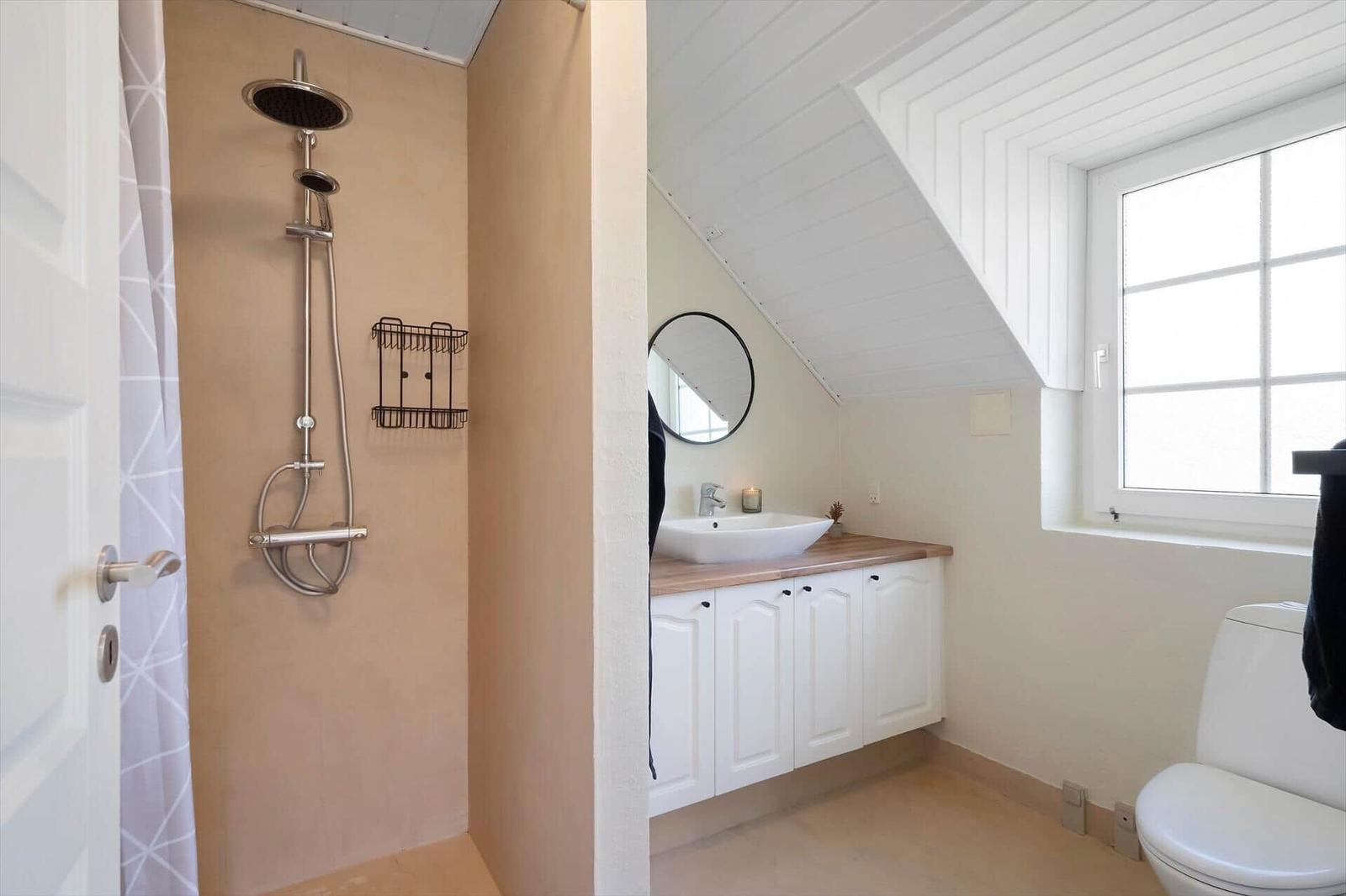 Dusche mit Duschbrause, Waschbecken mit Spiegel und Toilette in einem Dachbodenbad.
