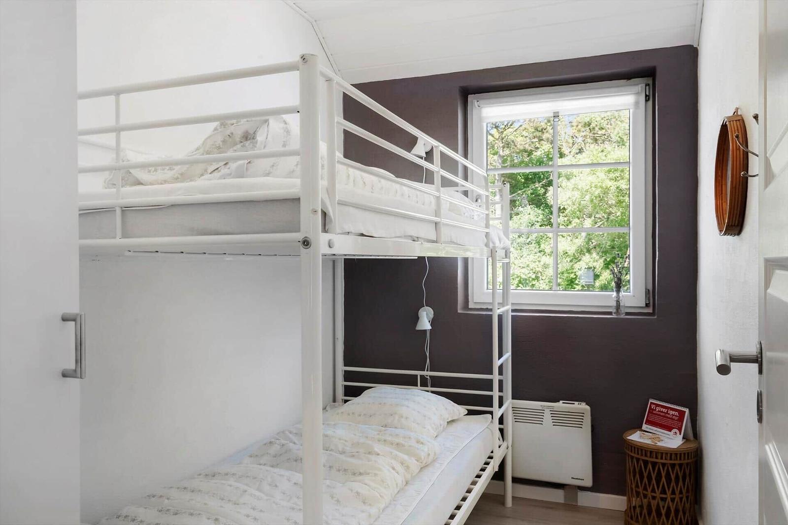 Zimmer mit Doppelstockbett, Fenster mit Blick auf Bäume und kleiner Tisch.
