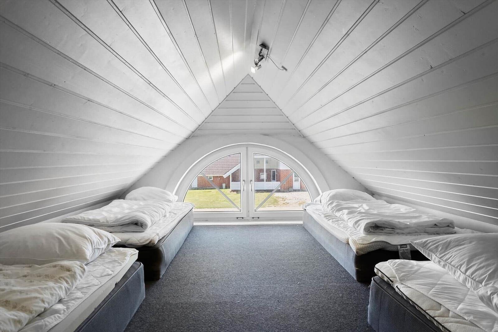 Zimmer mit drei Matratzen unter einem schrägen Dach und einer Bogenfensterfront.