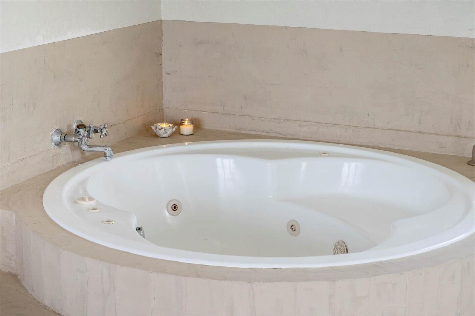 Eine runde Whirlpool-Badewanne mit Armaturen und Kerzen auf der Wand.