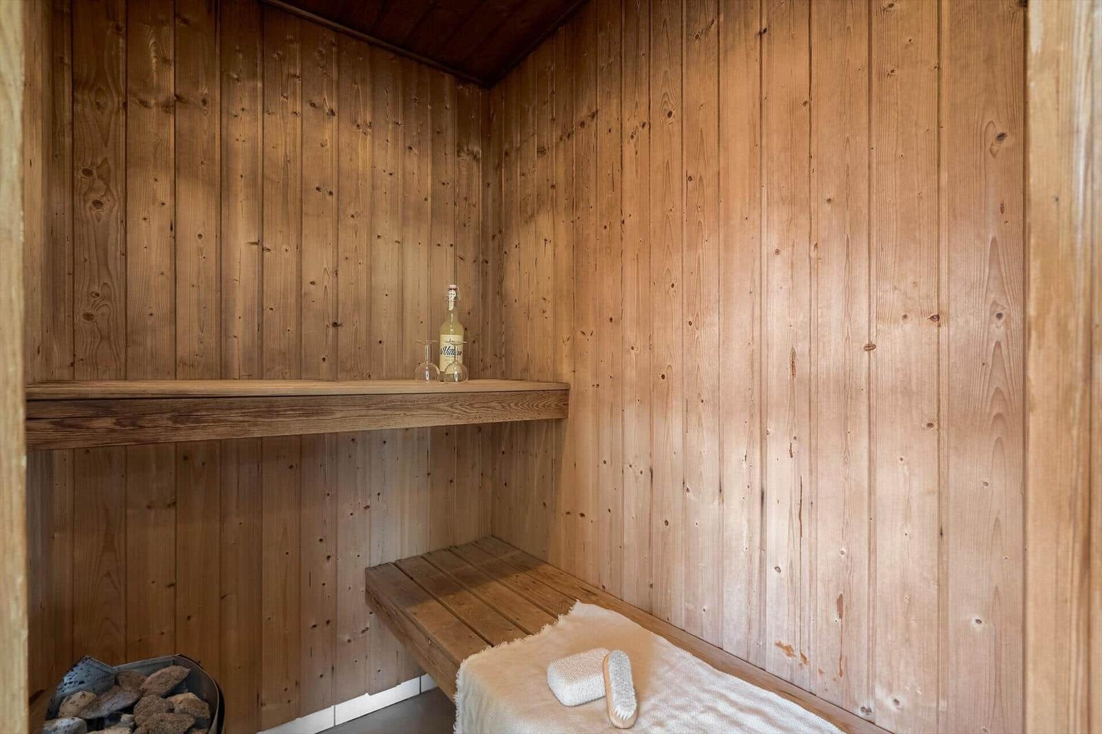 Holzsauna mit Bank, Flasche und Schwamm. Kamin mit Steinen.