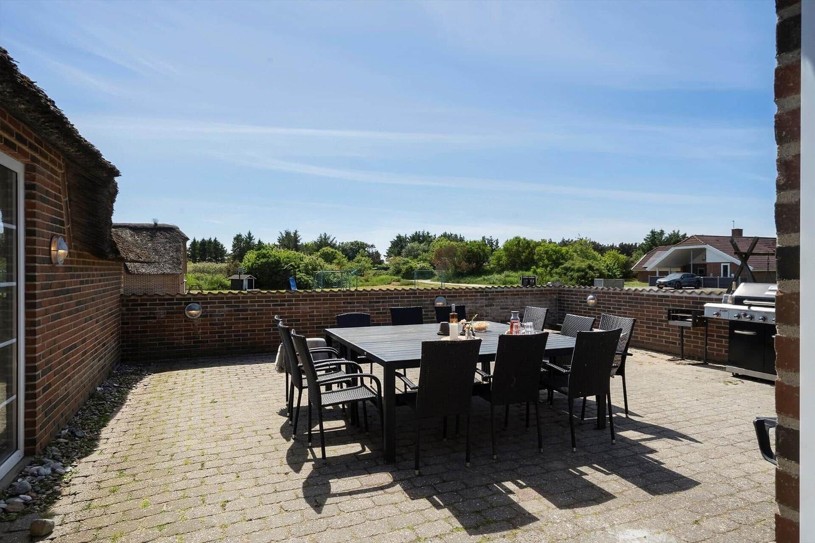 Terrasse mit Tisch, Stühlen und Grill. Blick auf grüne Landschaft.