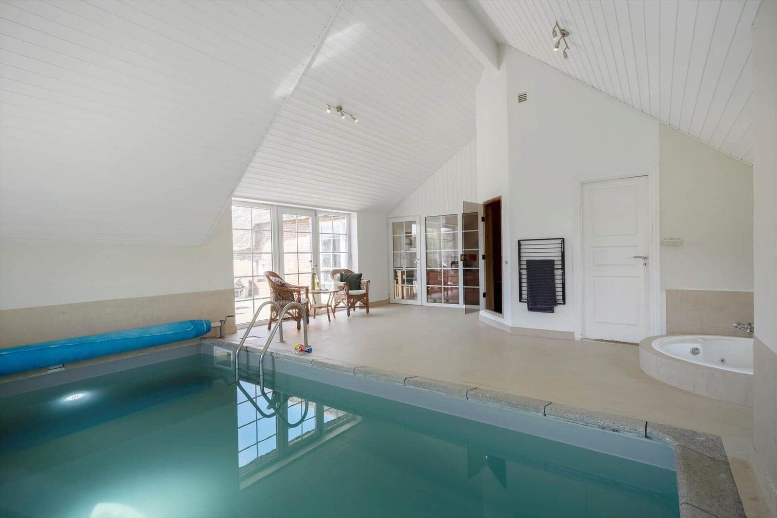 Indirekter Poolbereich mit Whirlpool und Sitzgelegenheit. Helle, geräumige Umgebung mit Fensterfront.