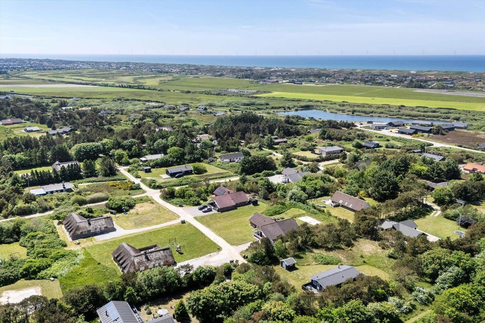 Luftbild von Ferienhäusern in grüner Landschaft mit Blick auf Meer und Windräder.