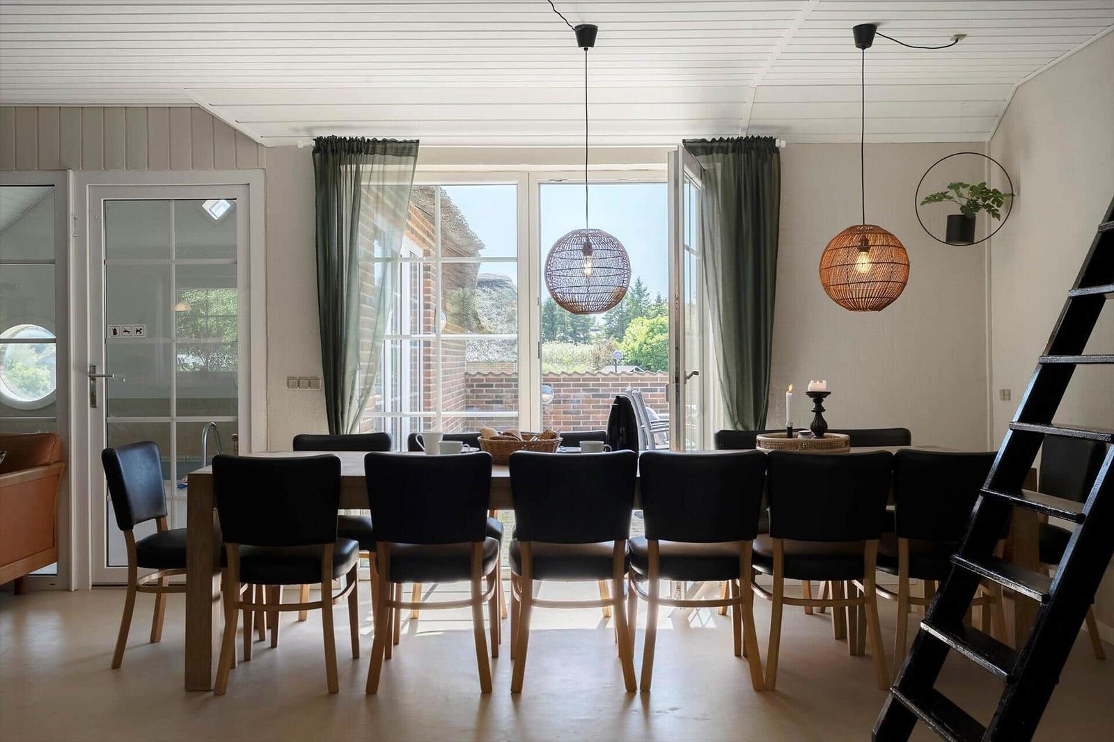 Esszimmer mit Tisch, Stühlen und Fenstern. Zwei Hängelampen und eine Leiter sind sichtbar.