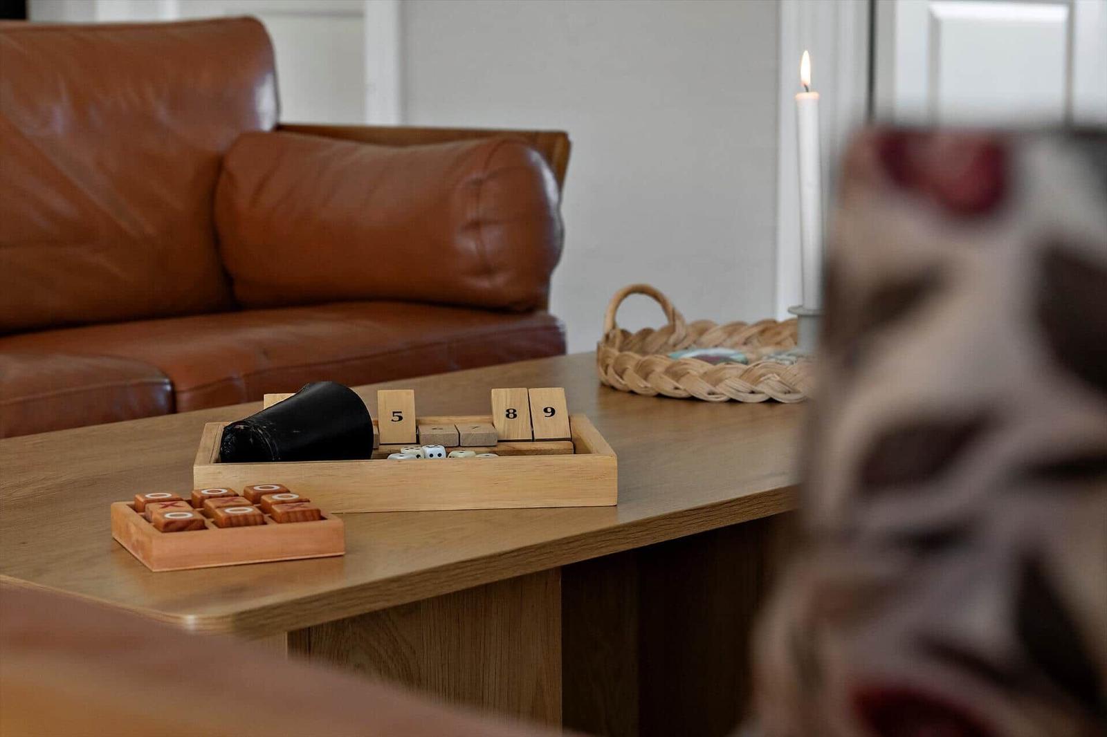 Holztisch mit Spielzeug, brauner Ledersofa und brennender Kerze im Hintergrund.
