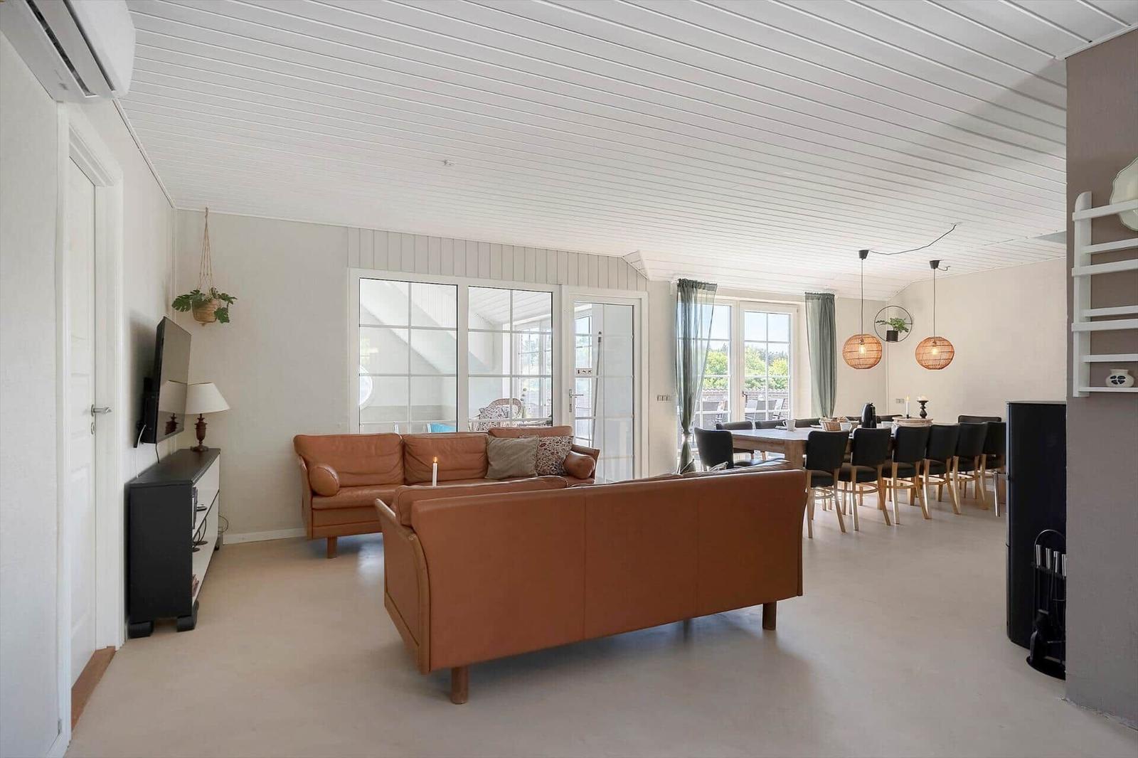 Wohn- und Essbereich mit braunen Sofas, Tisch und Stühlen. Weiße Decke und Fenster.