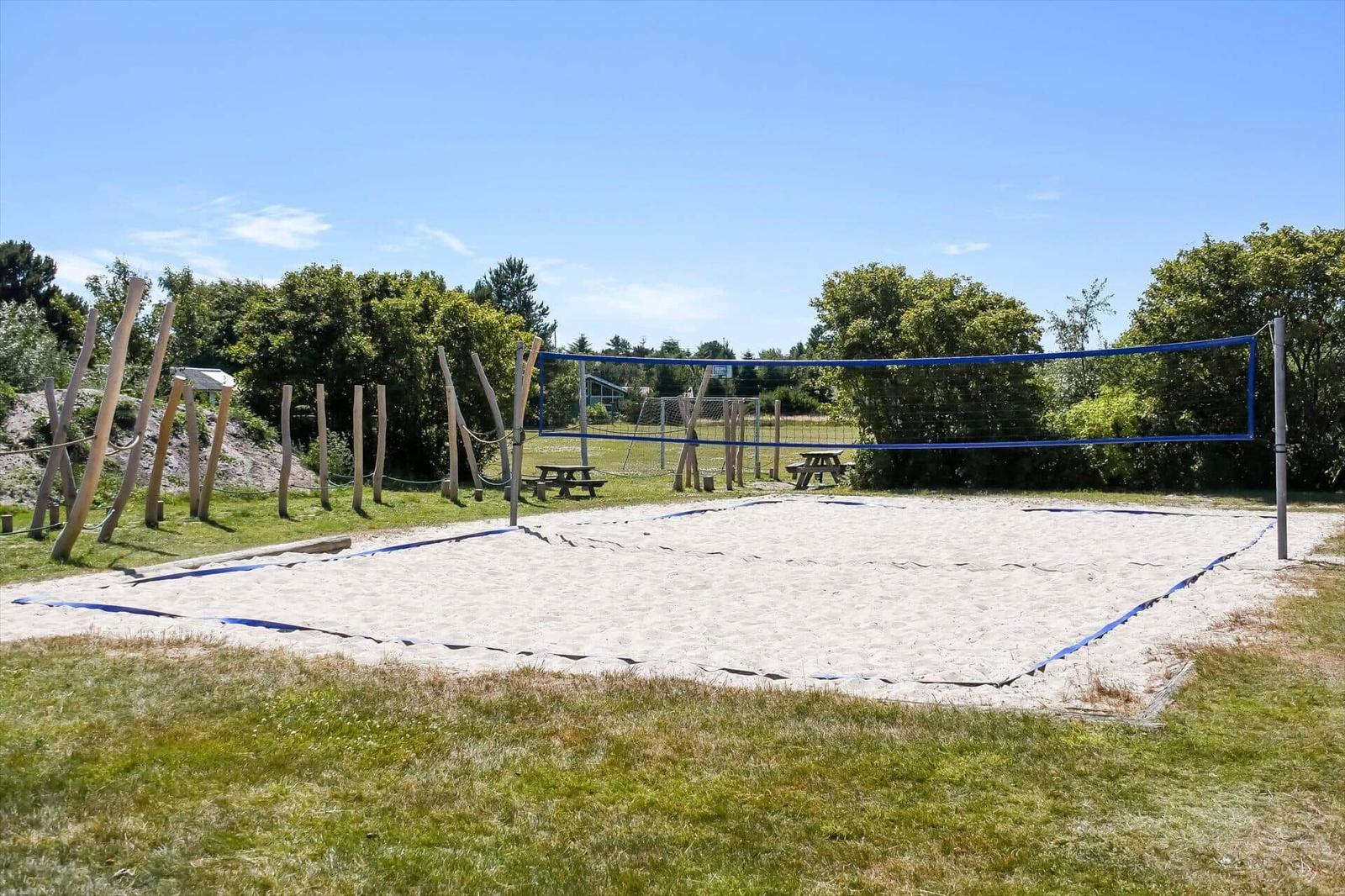 Sandplatz mit Volleyballnetz und Picknicktischen im Freien.