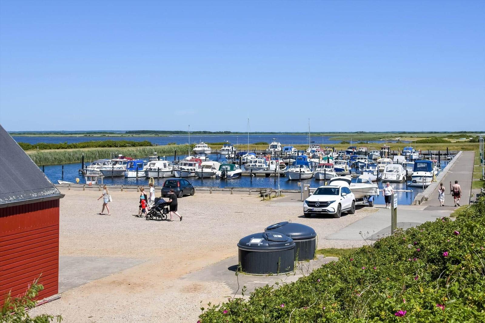 Hafen mit Booten, Parkplatz und rotem Gebäude im Vordergrund.