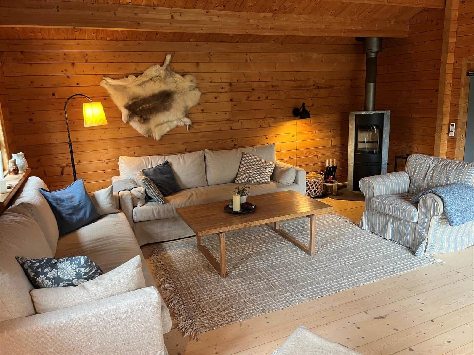 Wohnzimmer mit Holzwänden, Sofa, Sessel, Kamin und Fell an der Wand.