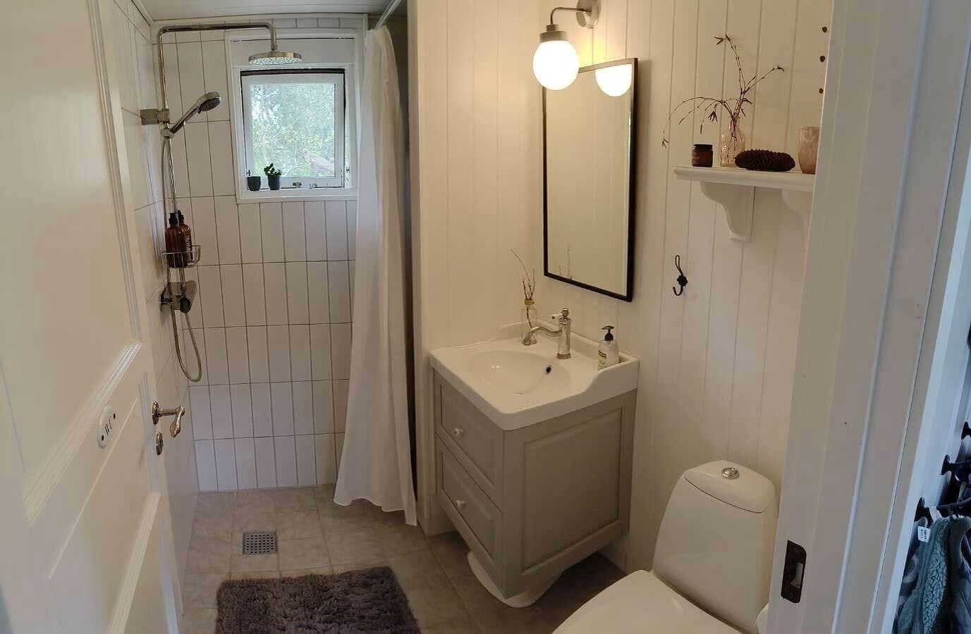 Badezimmer mit Dusche, Waschbecken und Toilette. Fenster mit Pflanzen.