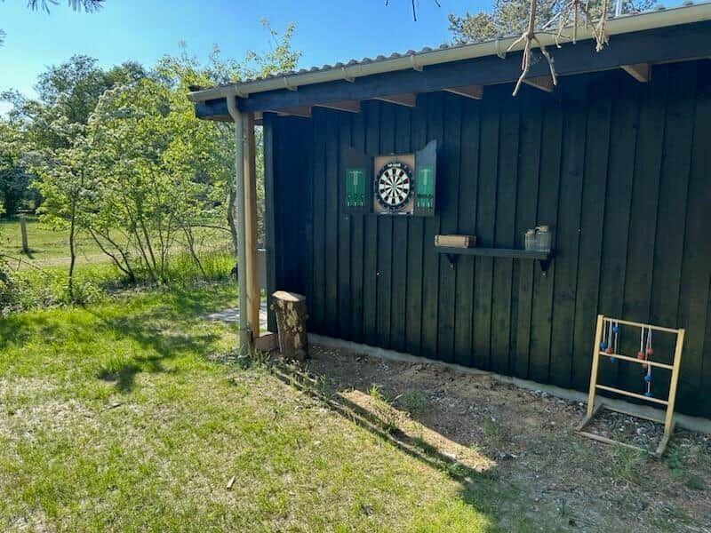 Außenbereich mit Dartscheibe an Holzwand, Holzständer und Grünfläche.