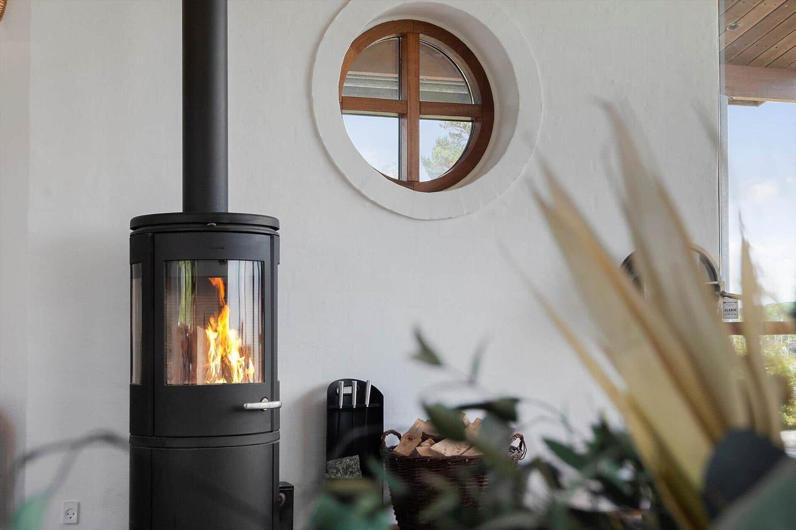 A wood-burning stove beside a round window on the wall.