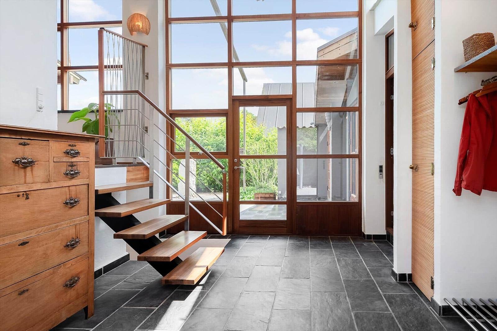 Entrance area with wooden staircase, large windows, and dark floor tiles.