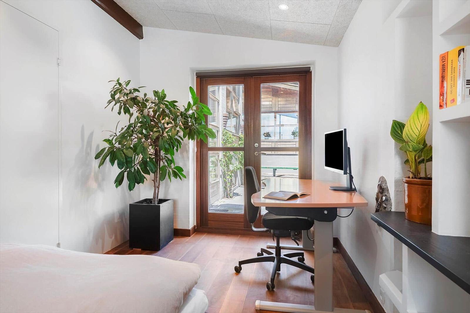 Bedroom with desk, plants, and door to balcony.