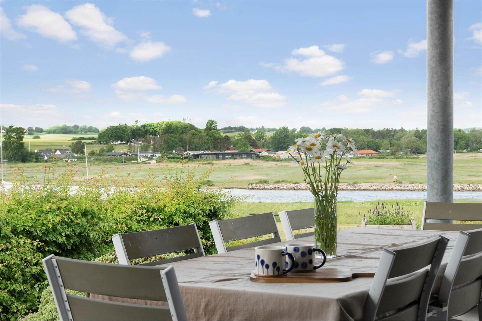 Table with chairs on terrace overlooking river and green fields.