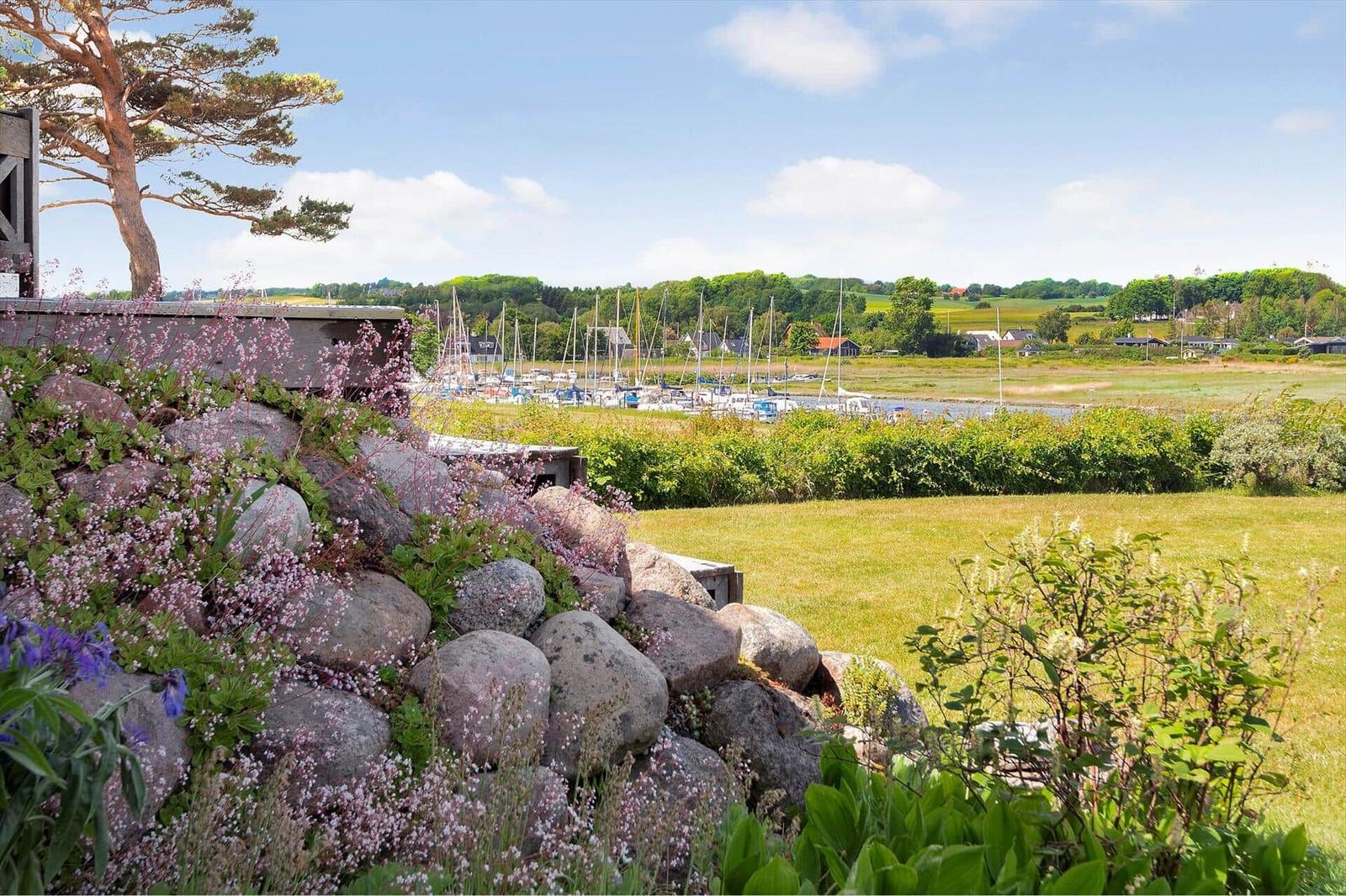 Garden with stone wall and flowers, view of harbor with boats and green landscape.