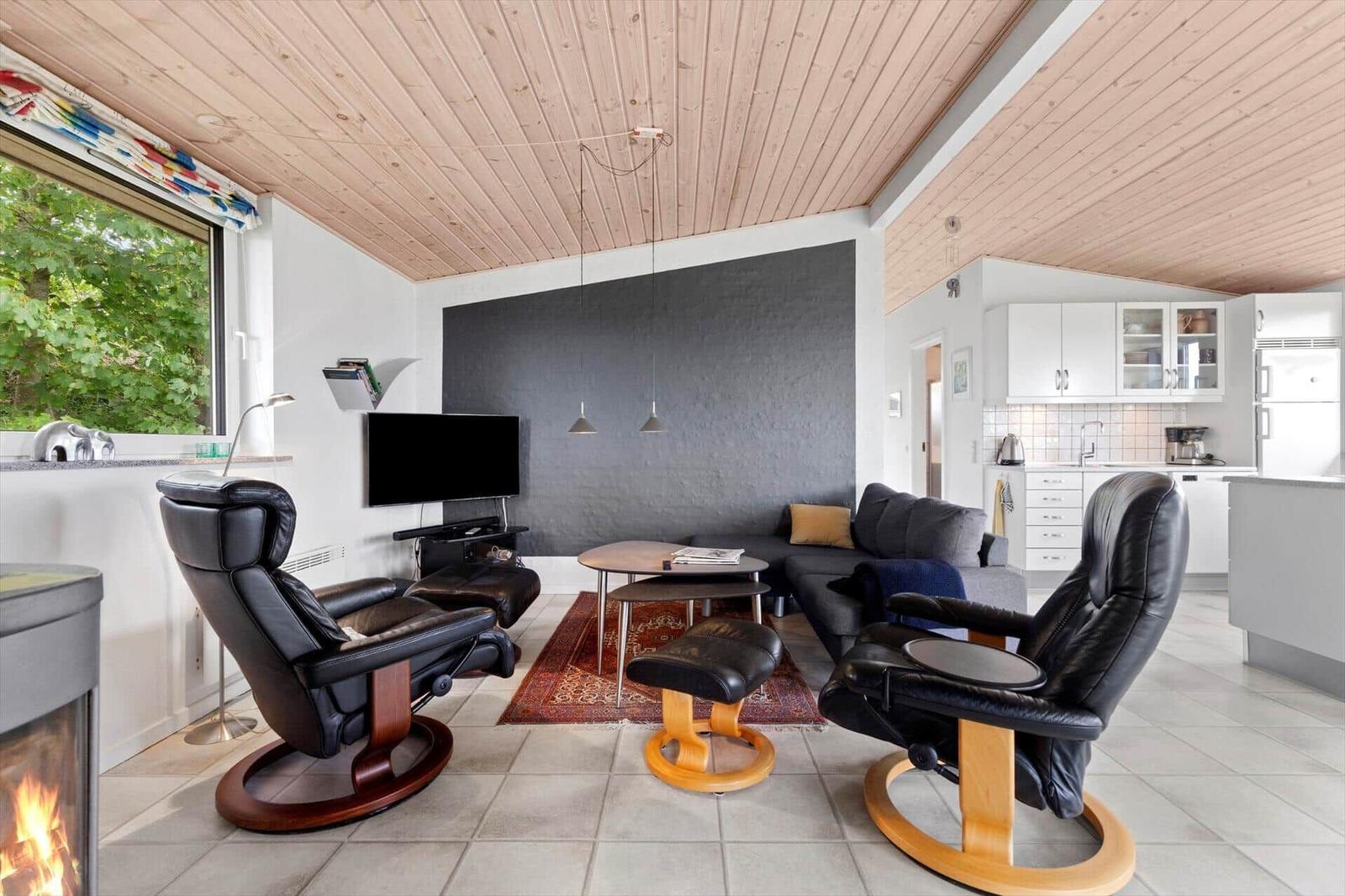 Living room with sofa, two black recliners, and fireplace. Kitchen is visible in the background.