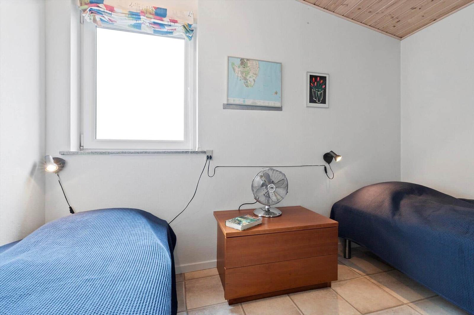 Room with two beds, nightstand, fan, and window with curtain.