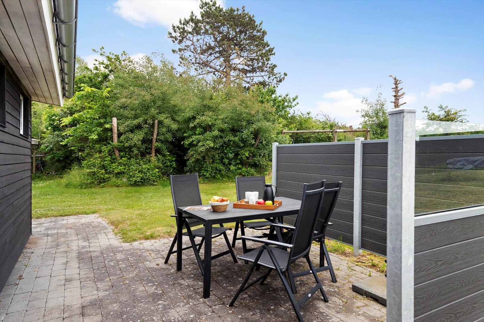 Terrace with table and chairs, surrounded by green garden and wooden fence.
