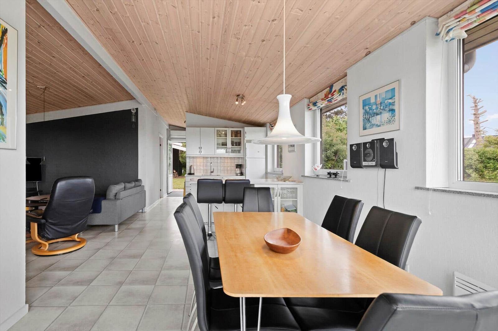 Dining area with wooden table and black chairs. Kitchen and living area are visible.