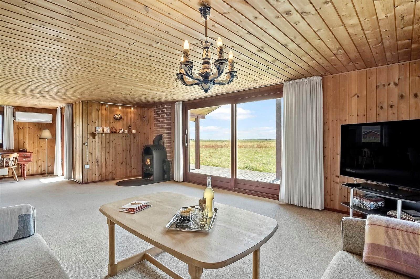 Wohnzimmer mit Holzwand, Kamin, TV und Blick auf eine Wiese.