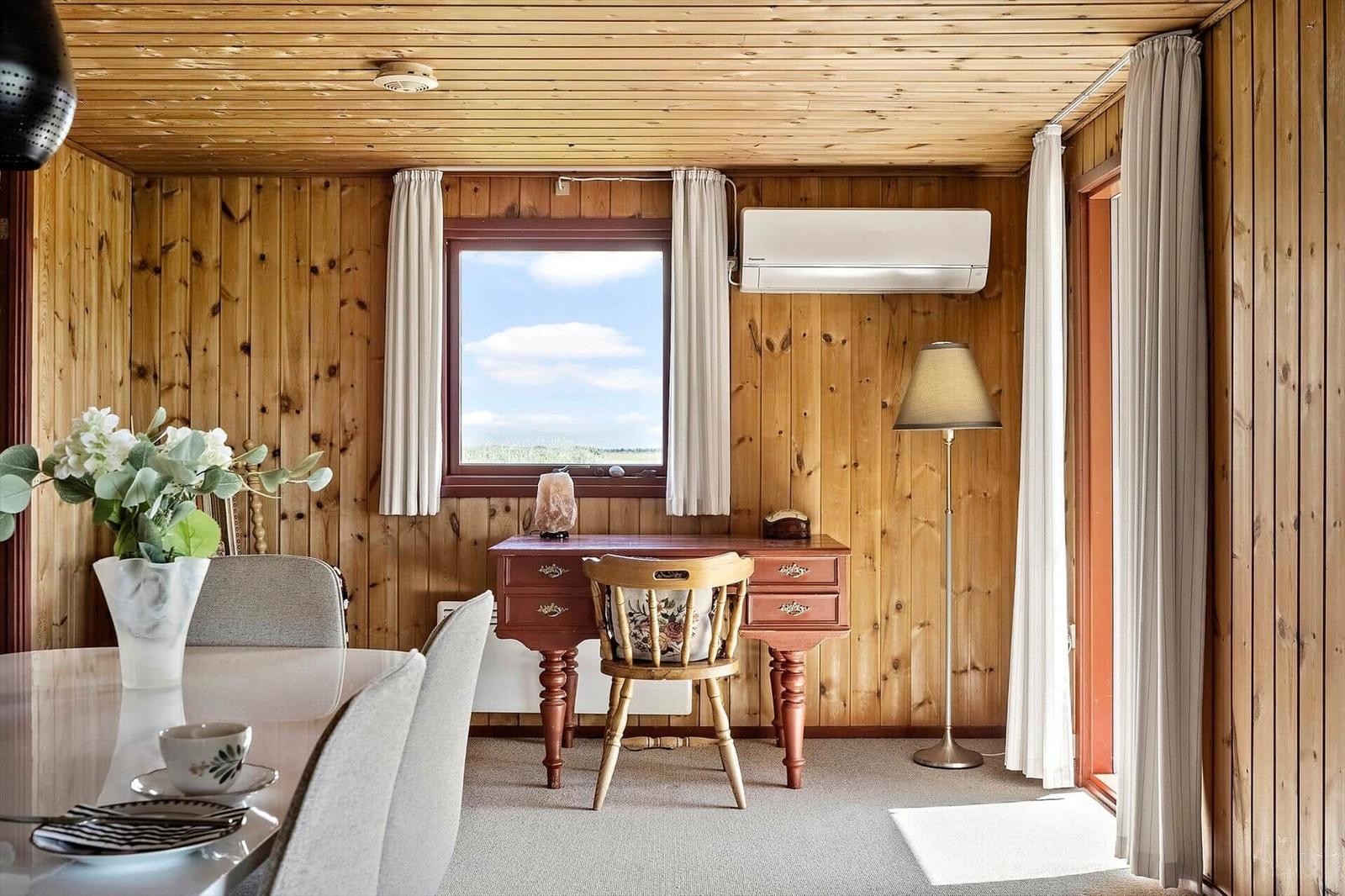 Raum mit Holzwänden, Schreibtisch, Stuhl, Fenster und Stehlampe.