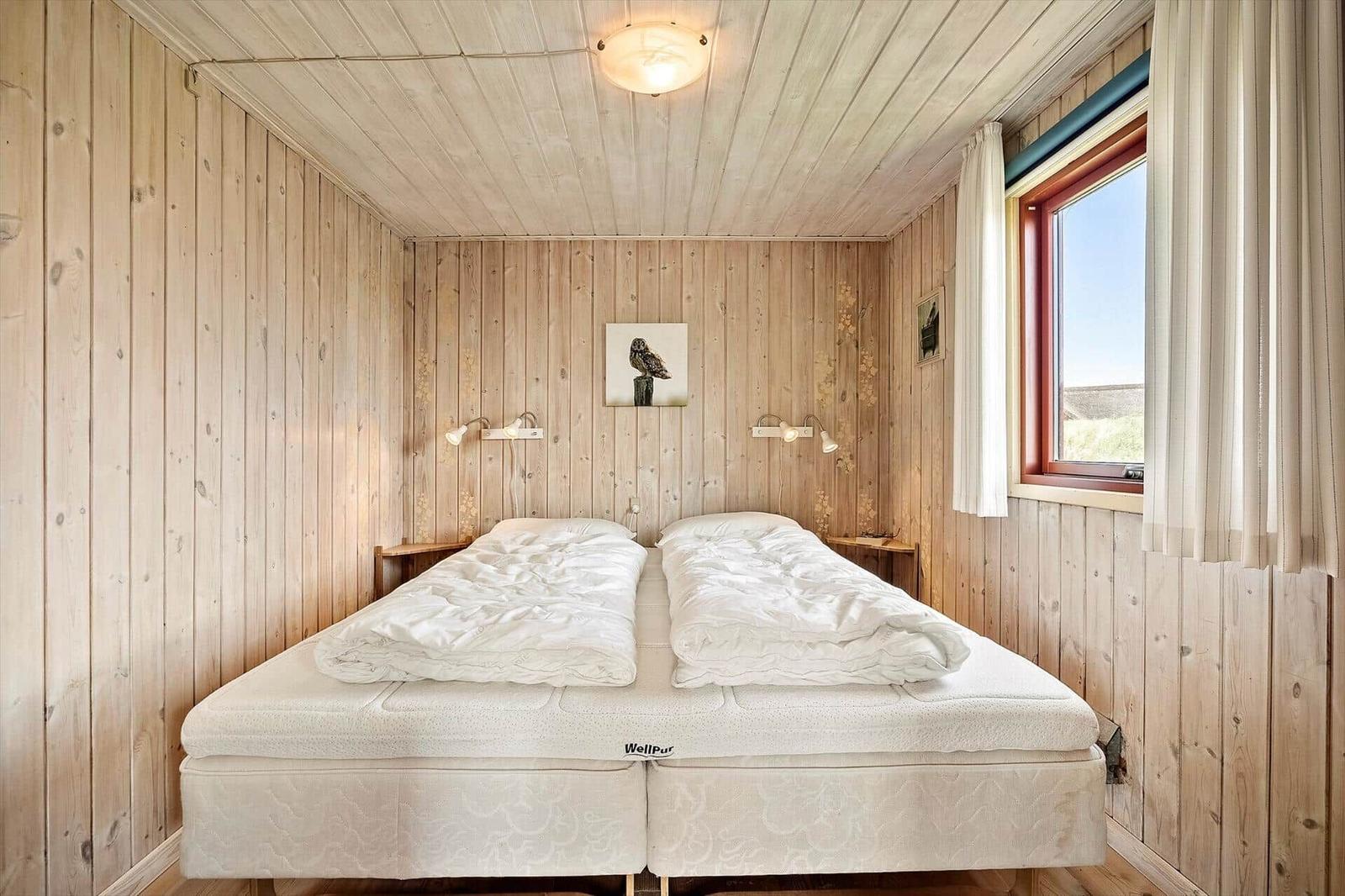 Schlafzimmer mit Holzwänden, Doppelbett und Fenster mit Blick.