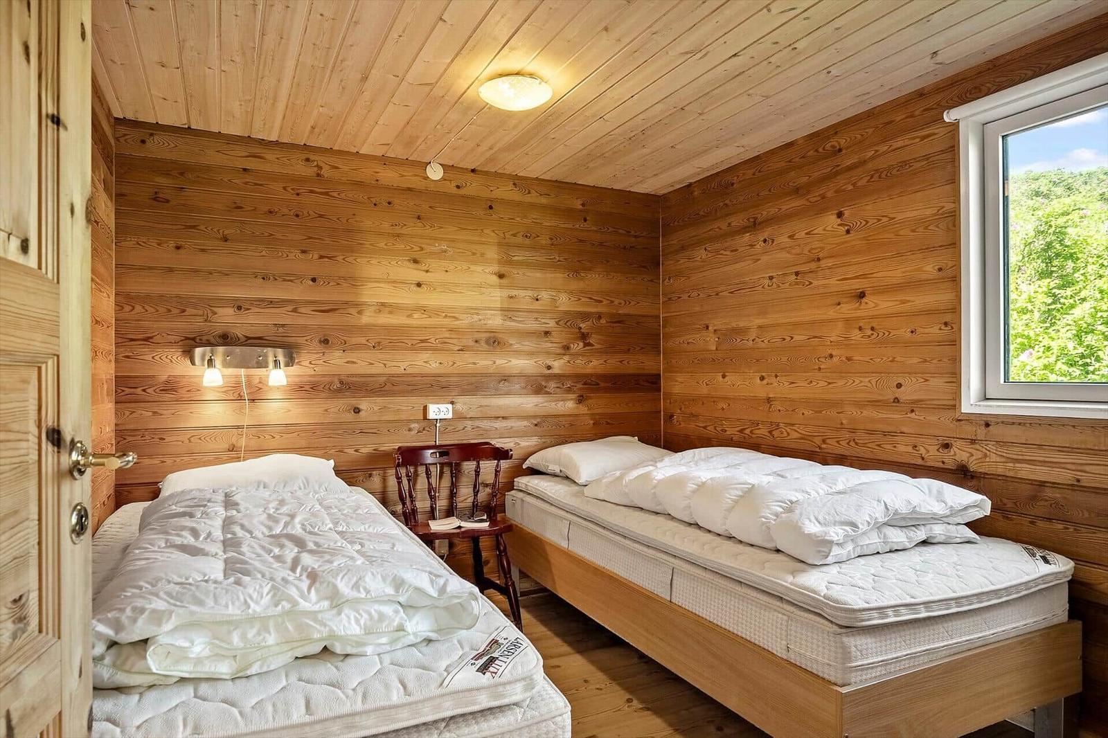 Zwei Einzelbetten in einem Holzhauszimmer mit Fenster und Nachttisch.