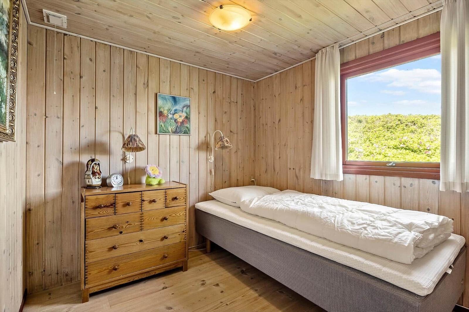 Schlafzimmer mit Holzwand, Bett und Fensterblick auf Grünflächen.