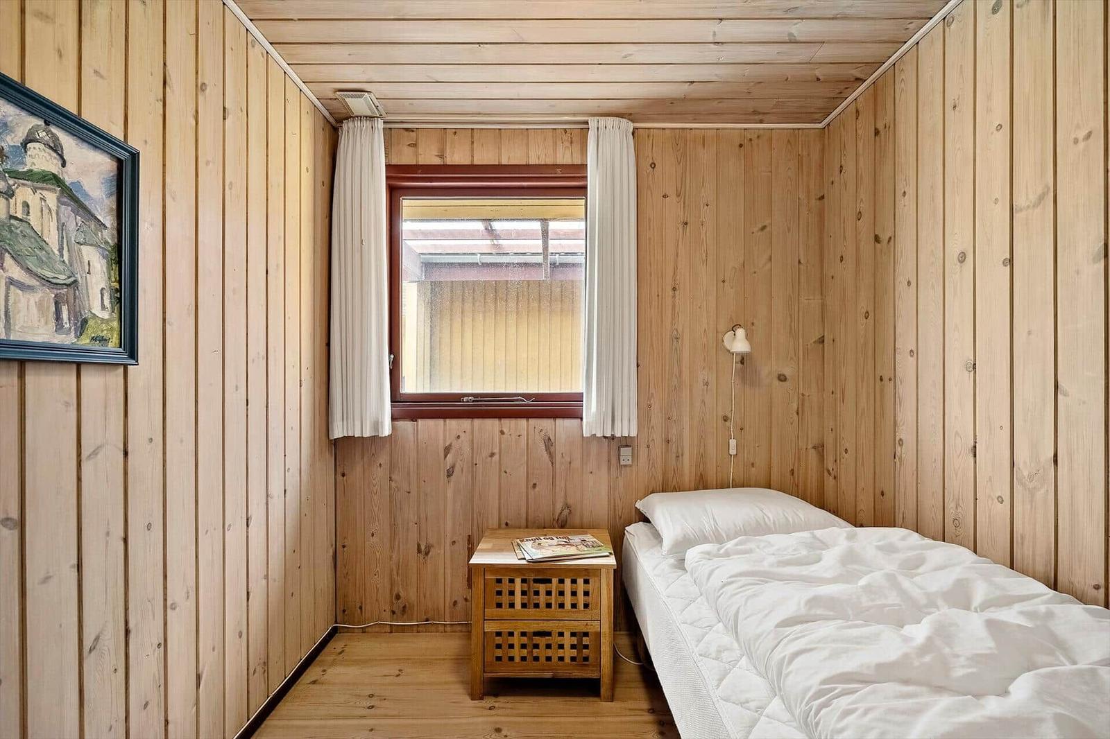 Ein Schlafzimmer mit Holzwänden, einem Bett, einem Nachttisch und einem Fenster.