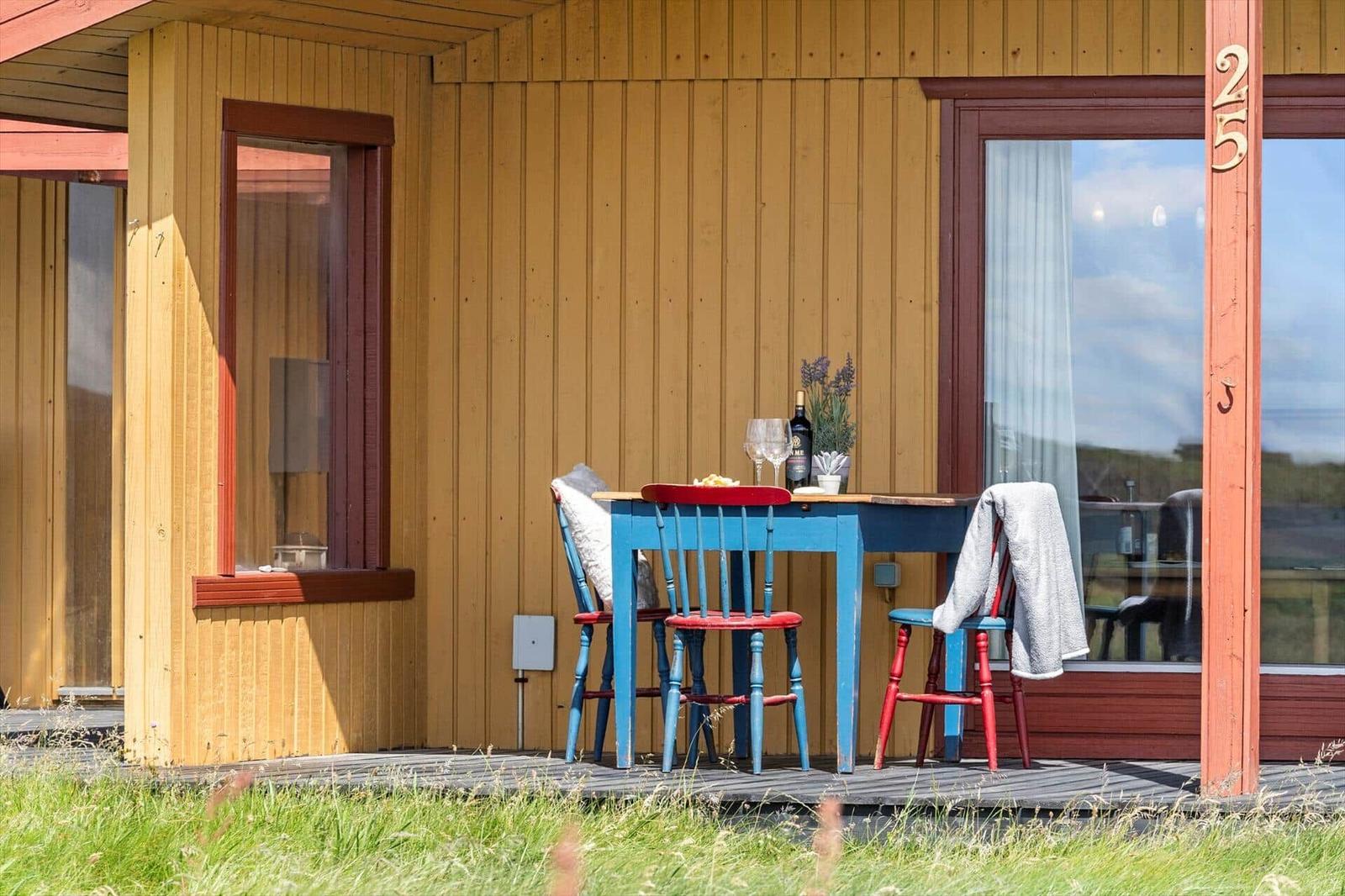 Terrasse mit blauem Tisch und roten Stühlen vor einem Holzhaus mit Fenstern.