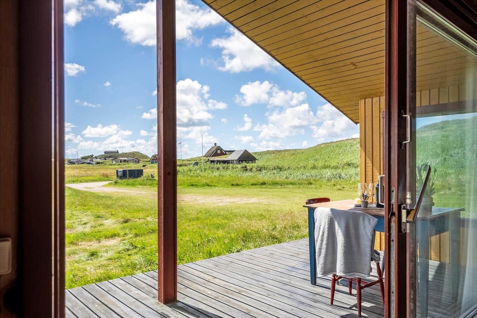Terrasse mit Tisch und Stühlen, Blick auf grüne Wiesen und Ferienhäuser.