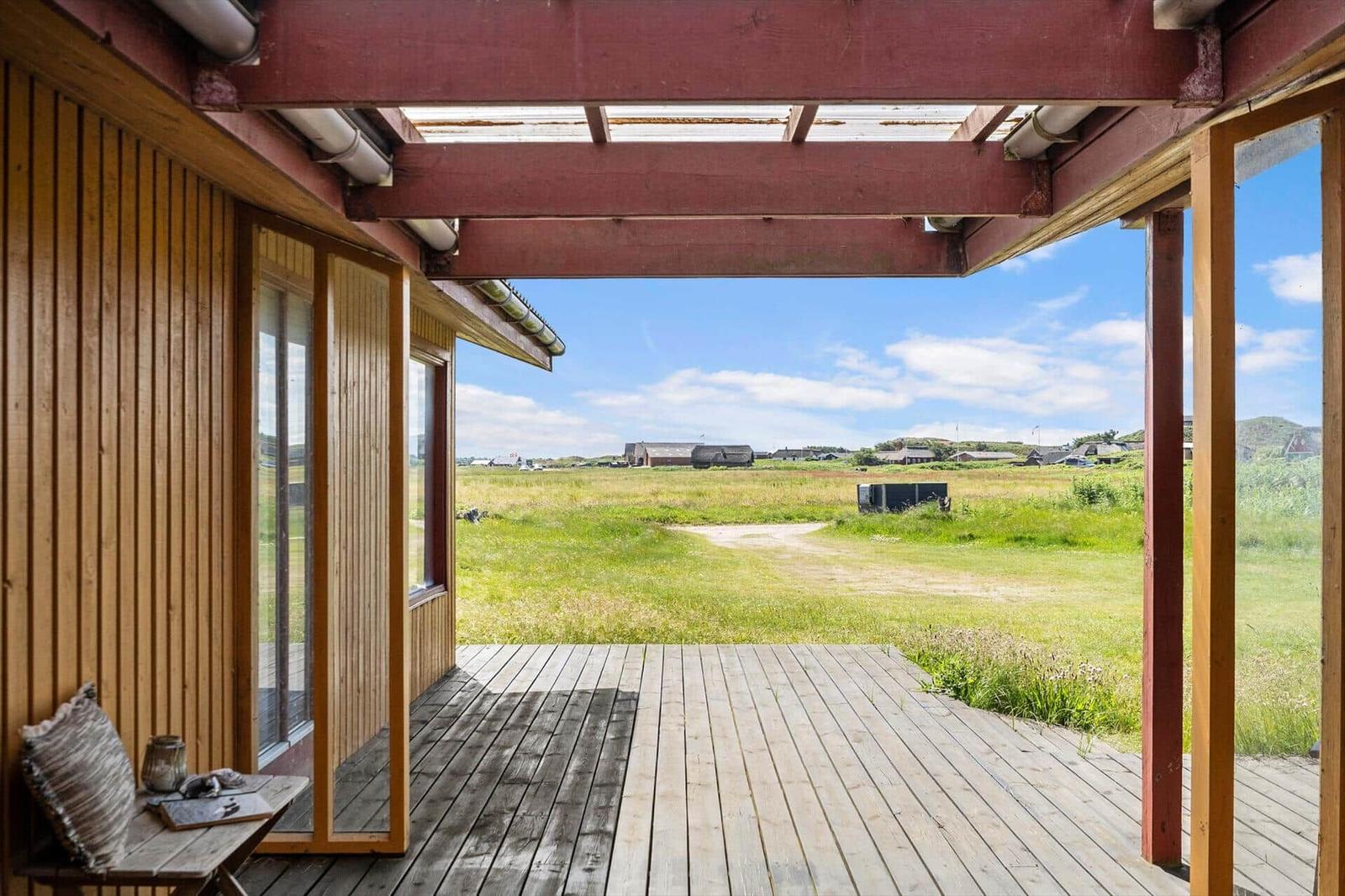 Terrasse mit Holzdecke und Blick auf grünes Feld und Himmel.