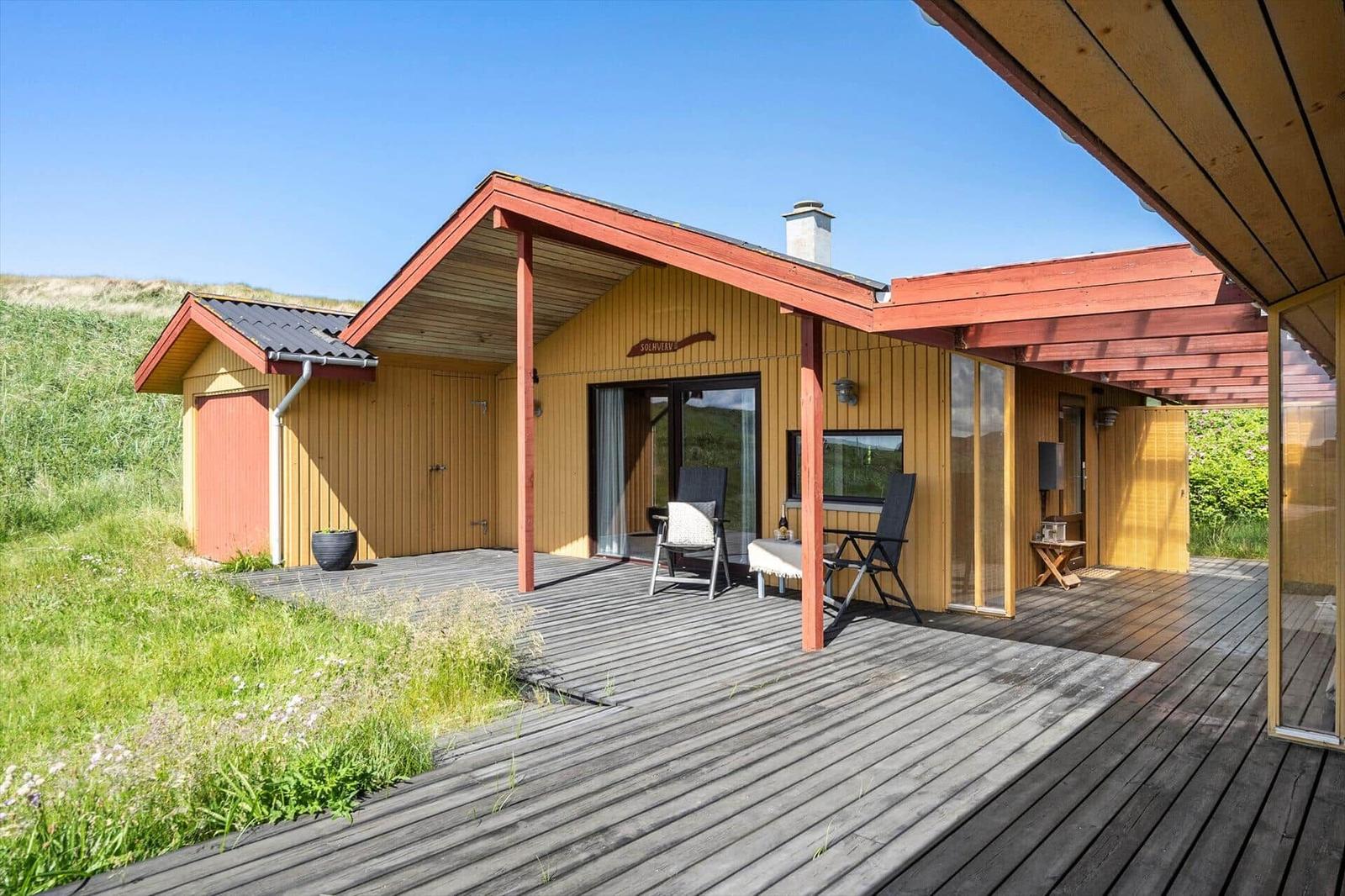 Holzhaus mit Terrasse und Garten. Außentisch, Stühle und Schornstein sichtbar.