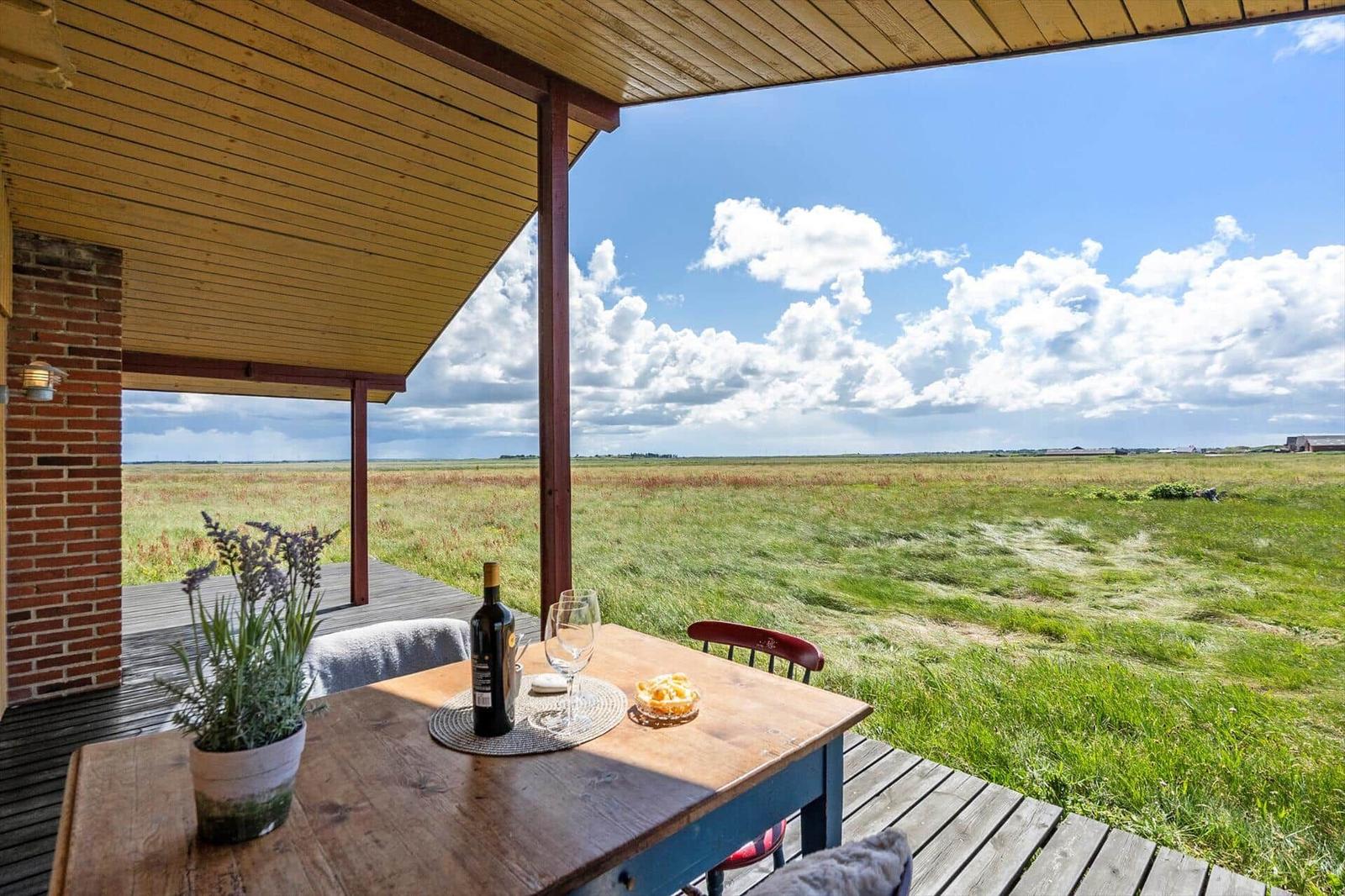 Terrasse mit Tisch, Wein und Lavendel. Blick auf grünes Feld unter blauem Himmel.