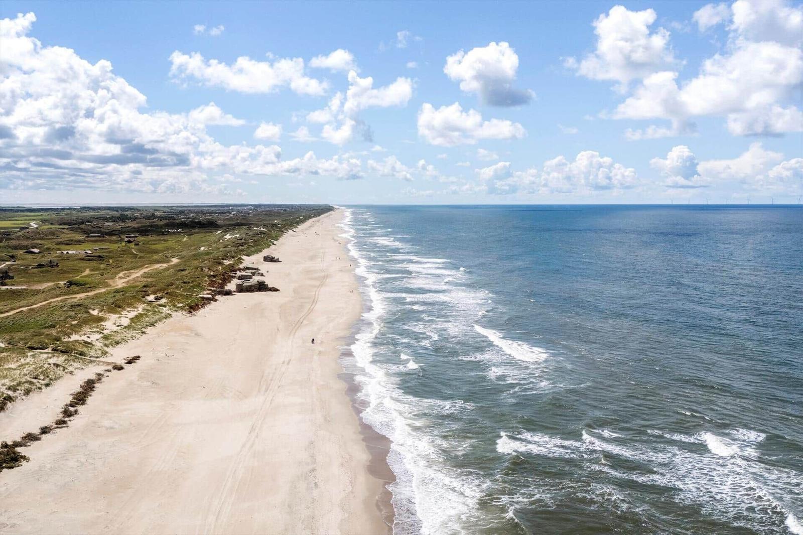 Strand mit Sand und Wellen unter blauem Himmel mit weißen Wolken.