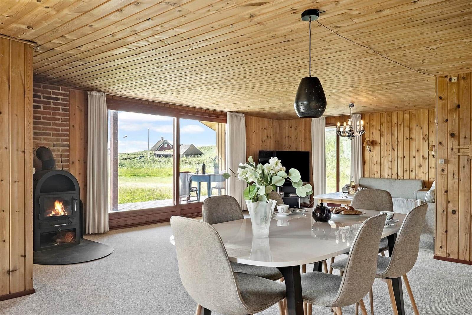 Essbereich mit Esstisch und Stühlen, Kamin und Blick auf grüne Landschaft.