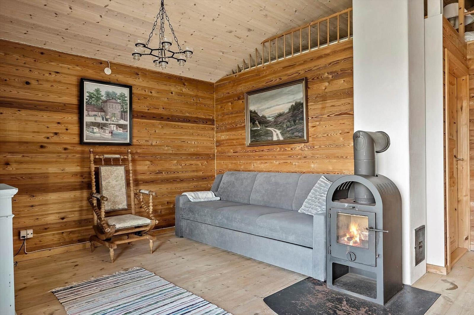 Wohnzimmer mit Holzwand, Sofa, Kaminofen und Stuhl.