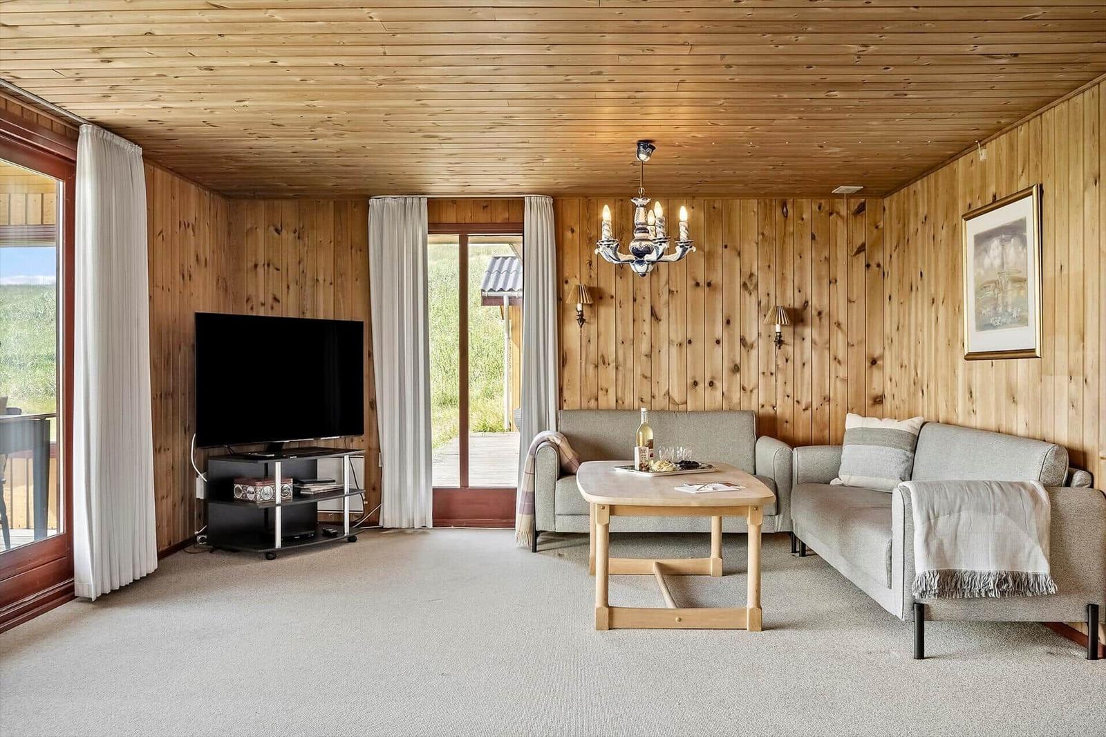 Wohnzimmer mit Holzwand, Sofa, Couchtisch und Fernseher. Türen führen nach draußen.