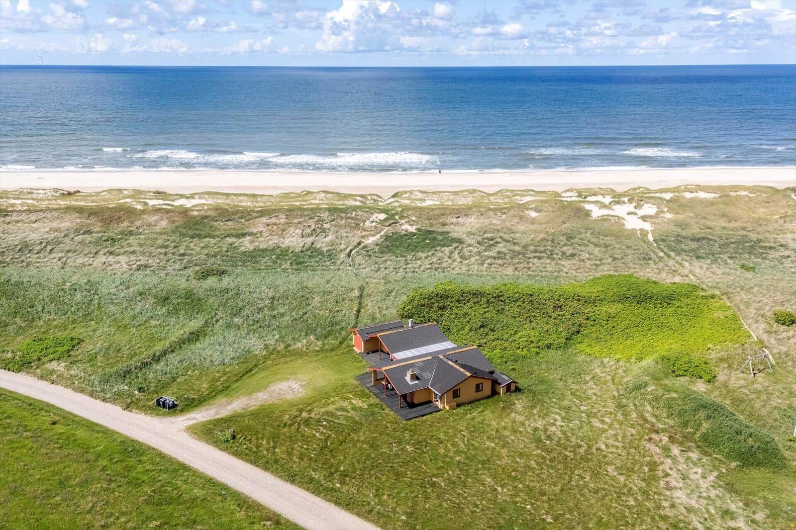 Haus mit Terrasse auf grüner Wiese, Strand und Meer im Hintergrund.