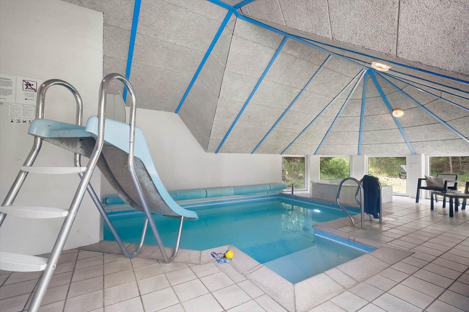 Innere Schwimmhalle mit Rutsche, Pool und Sitzgelegenheiten.