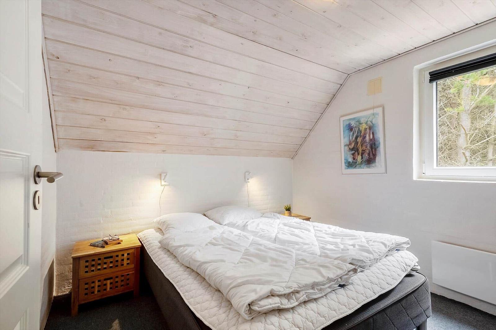Schlafzimmer mit Doppelbett, Holzdecke und Fenster zur Natur.
