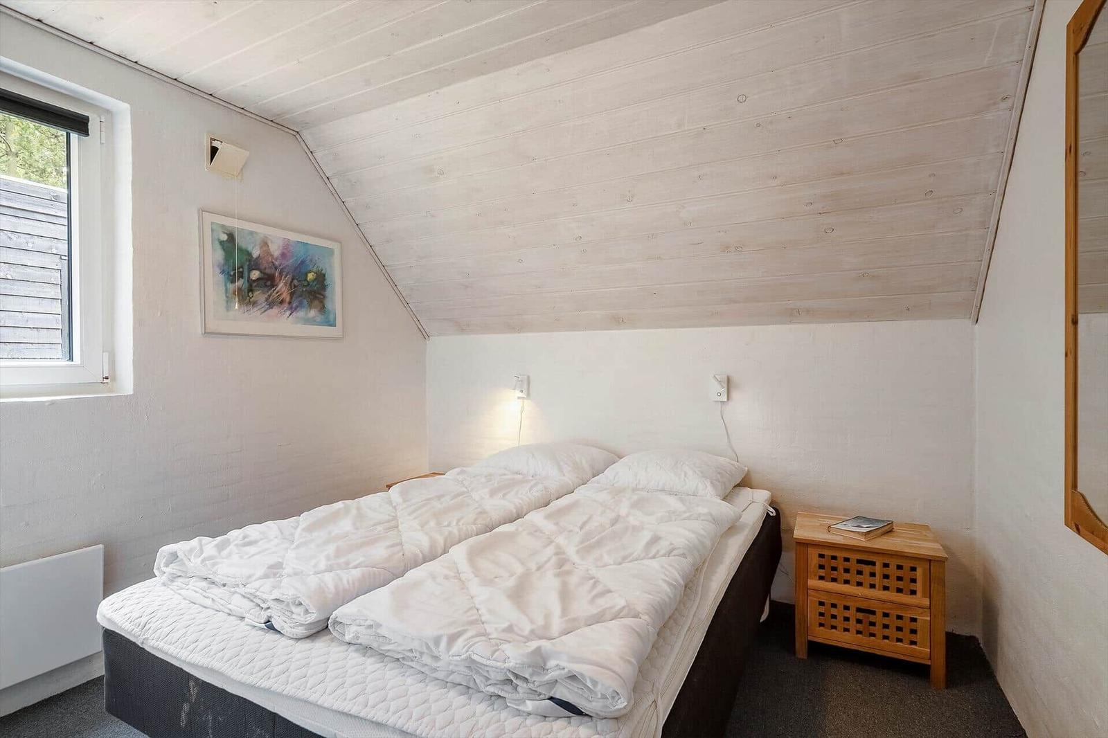Schlafzimmer mit Dachschräge, Bett, Nachttisch und Fenster.