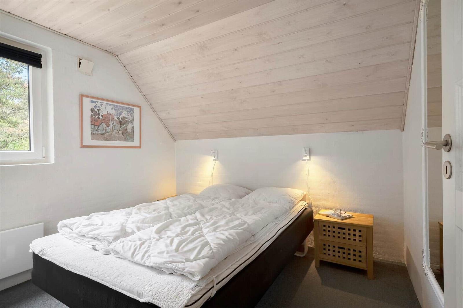 Schlafzimmer mit Bett, Nachttisch und Fenster. Holzdecke und Wandbild.