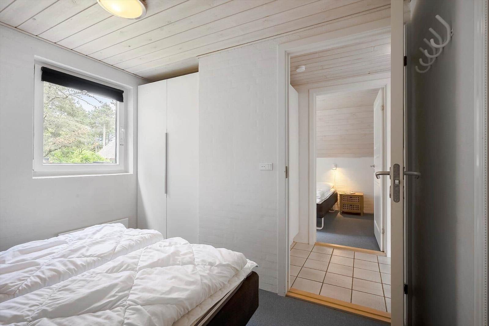 Schlafzimmer mit Bett, Kleiderschrank und Fenster. Durchgang zu weiterem Raum mit Bett.