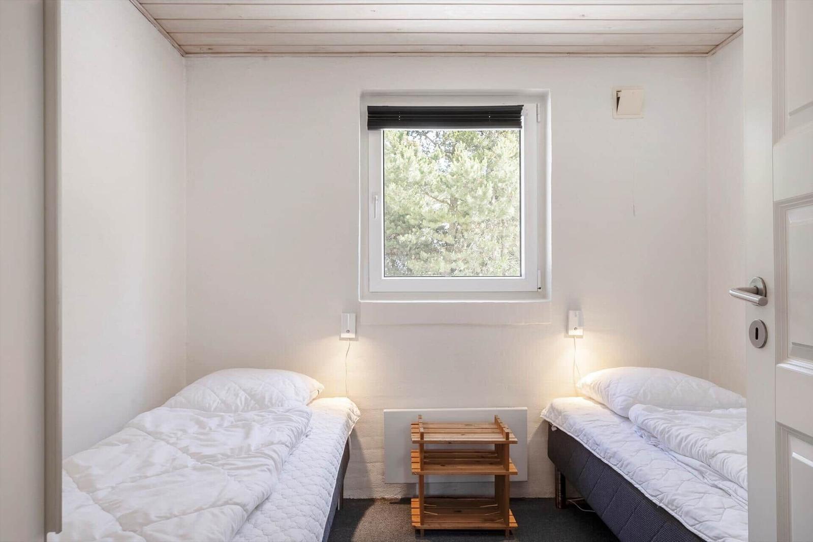 Zwei Einzelbetten mit weißer Bettwäsche, kleiner Holztisch und Fenster mit Blick auf Bäume.