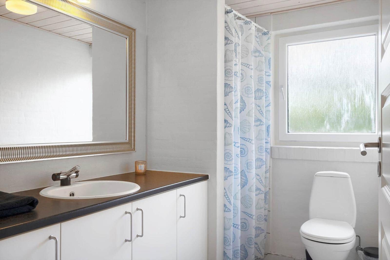 Bad mit Waschbecken, Spiegel und Toilette. Duschvorhang mit Muschelmotiv.