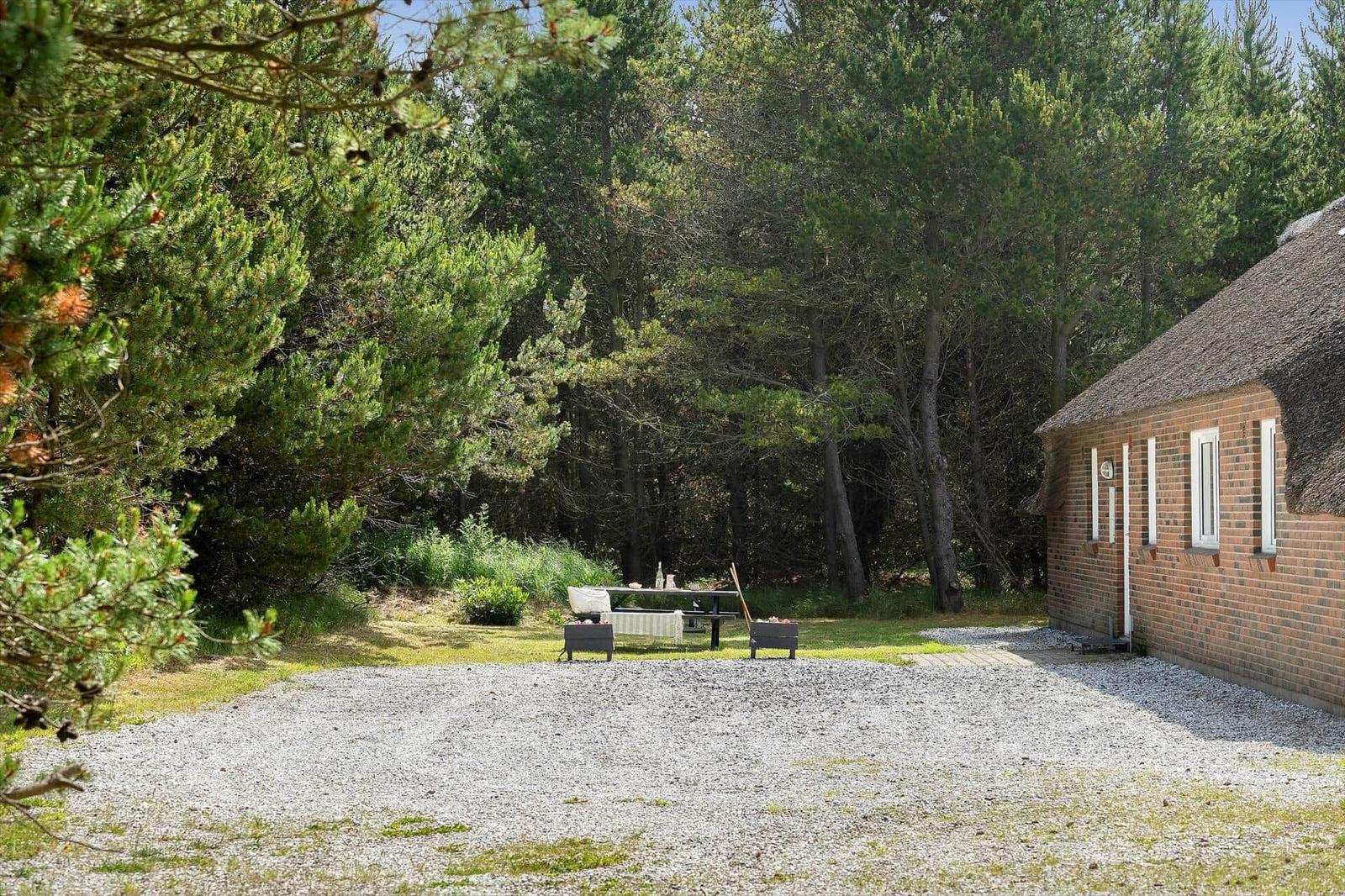 Haus mit Schilfdecke, Garten mit Tisch und Stühlen, umgeben von Bäumen.