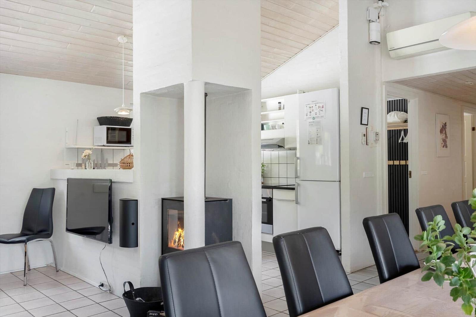 Küche mit Kühlschrank, Esstisch mit Stühlen und Kamin im Wohnbereich.